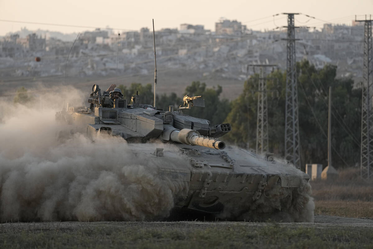 With destroyed buildings in the Gaza Strip behind him, an Israeli soldier waves from a tank, ne ...