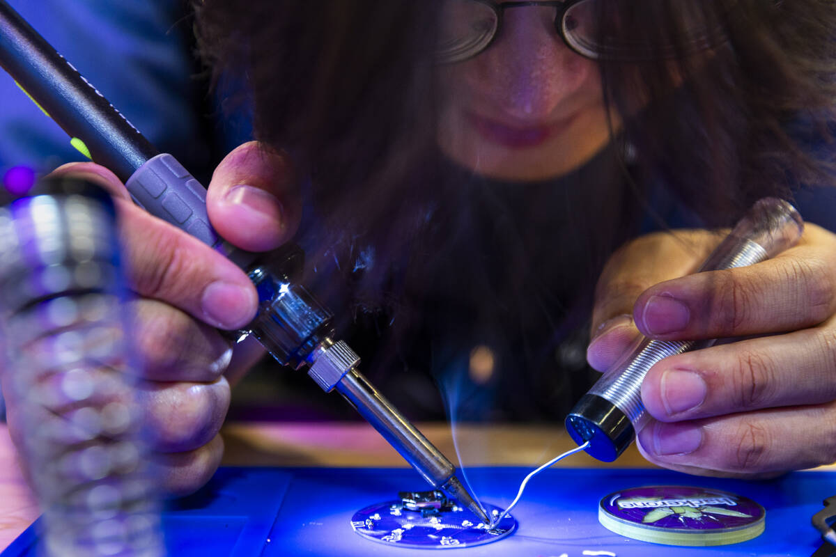 Attendee Forrest McMahon solders an electronic button in the HackerOne display during the Black ...