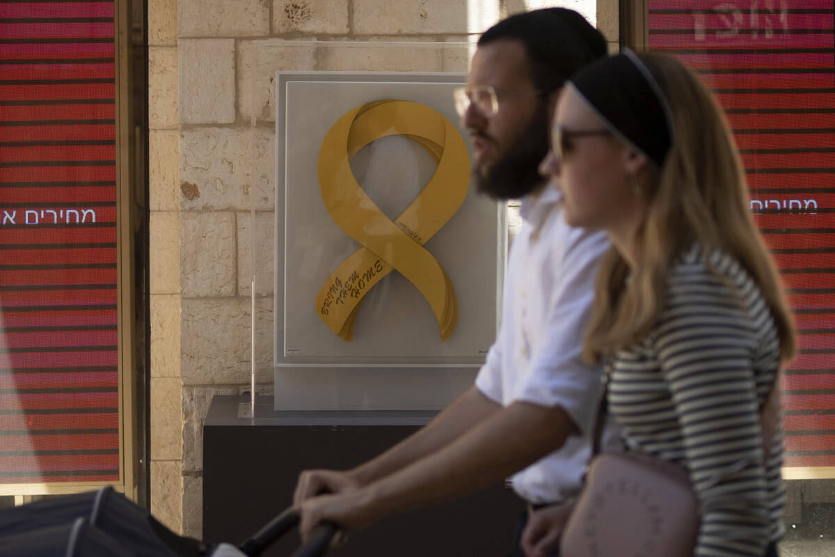 A couple stroll past artwork displayed in a pedestrian mall showing a yellow ribbon calling for ...