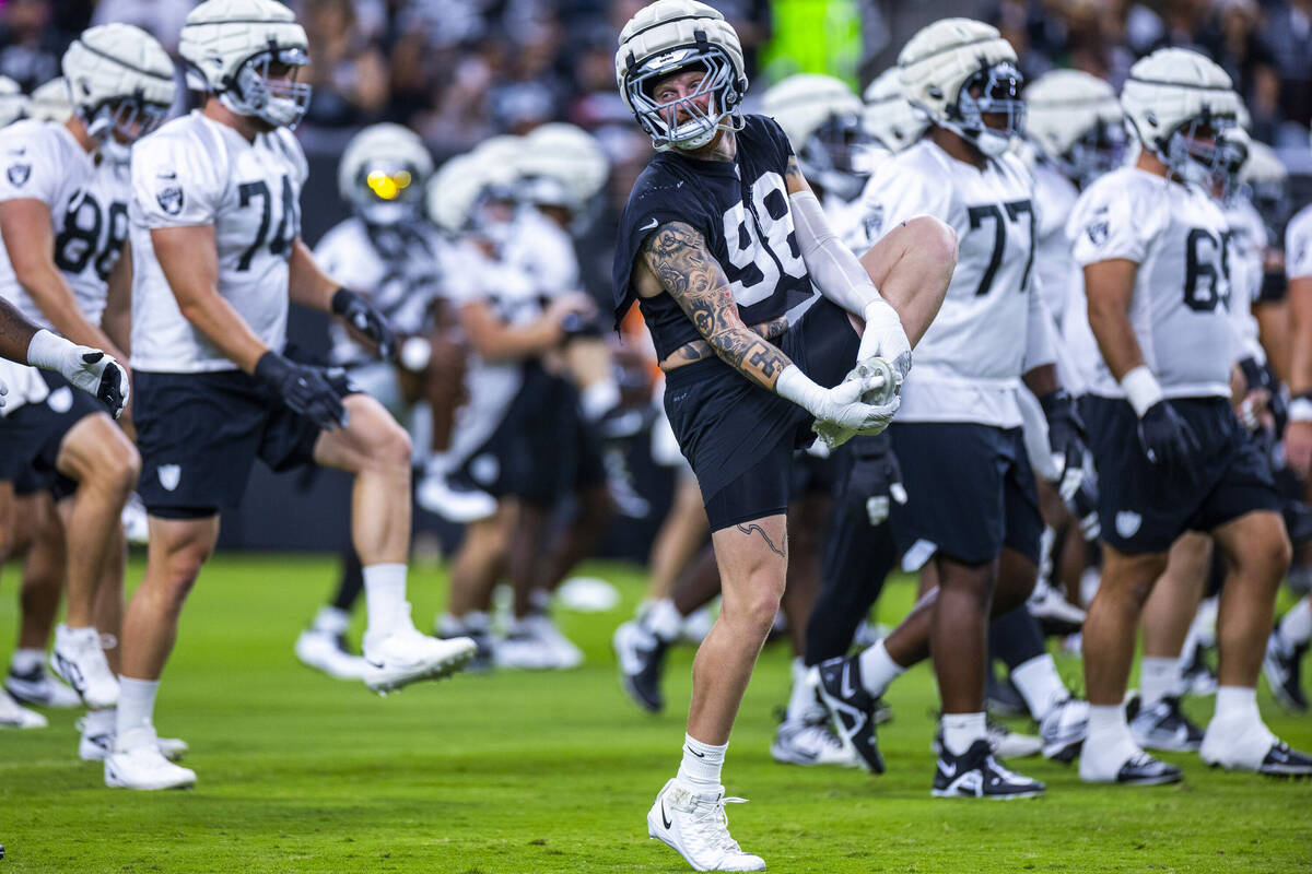 Raiders defensive end Maxx Crosby (98) smiles at a teammate while stretching during an open pra ...