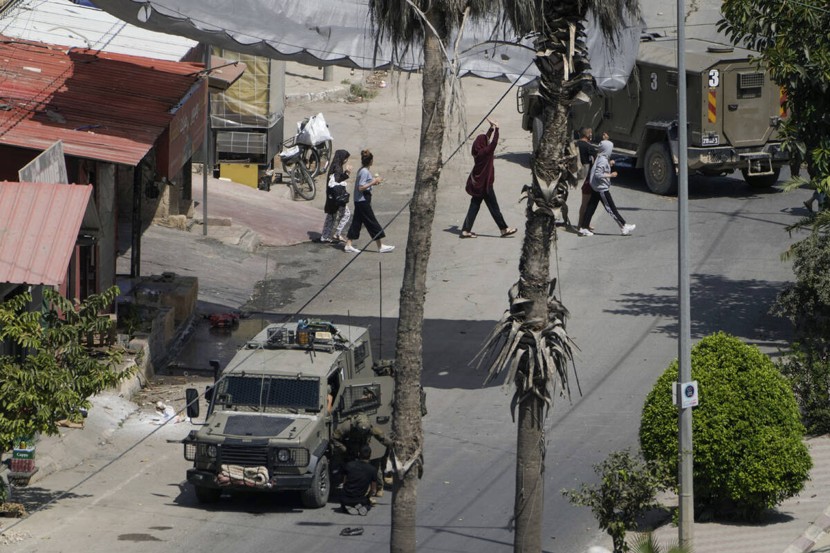 Israeli soldiers arrest a Palestinian man as others walk by with their hands up during a milita ...