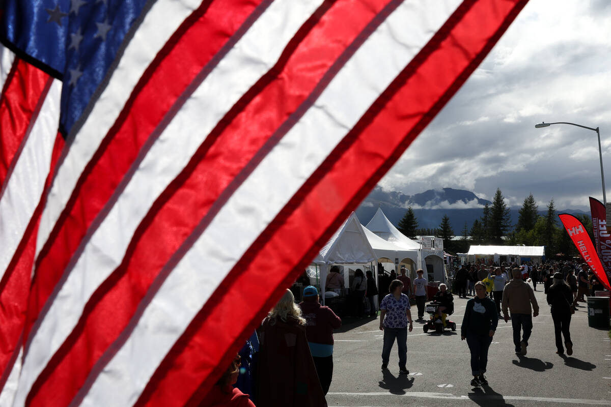 Fairgoers walk the grounds past an American flag during the Alaska State Fair on Thursday, Aug. ...