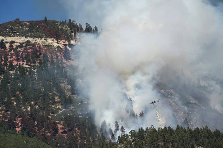 A helicopter drops water as the Davis Fire continues to burn in the mountains south of Reno, Ne ...