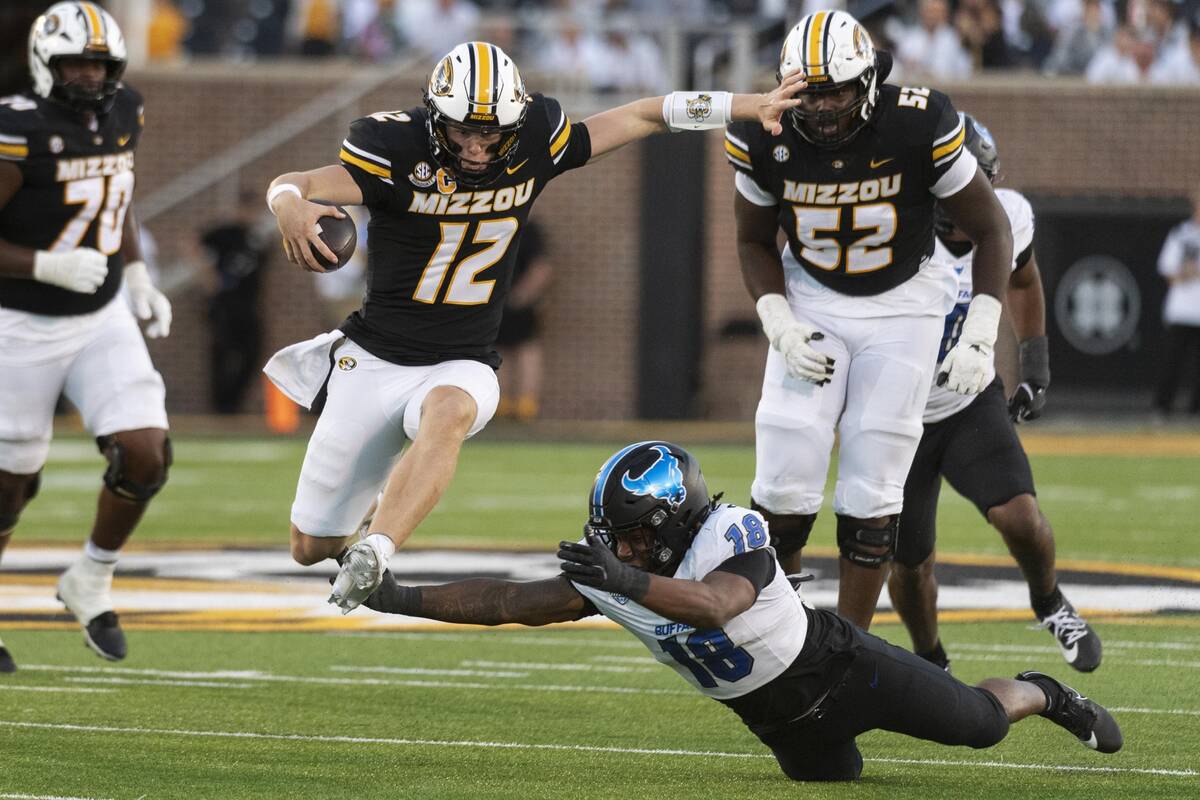 Missouri quarterback Brady Cook (12) leaps over Buffalo linebacker Dion Crawford (18) as he run ...