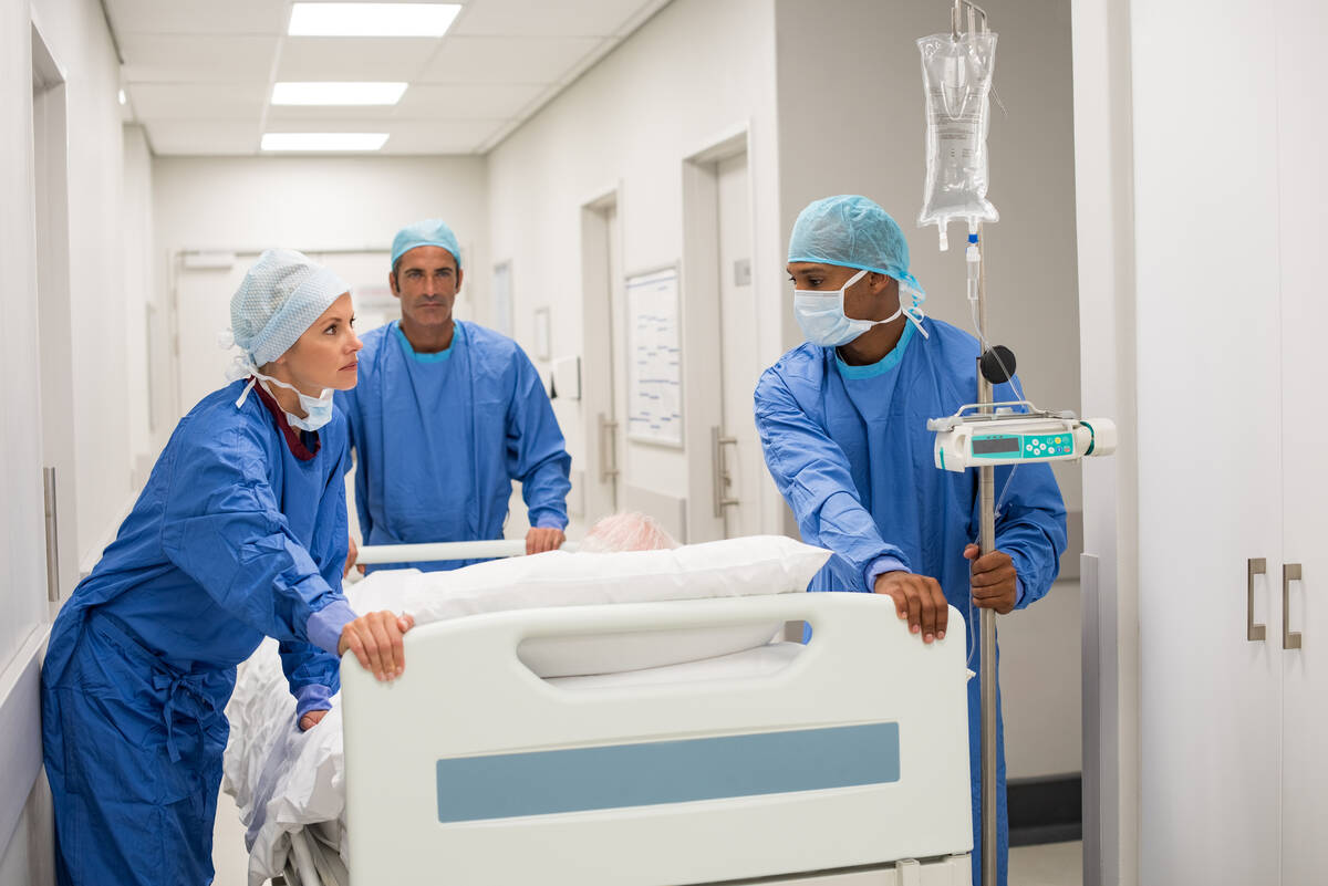 Patient hospital bed moved by medical staff to operating room. Surgeons pushing patient on bed ...