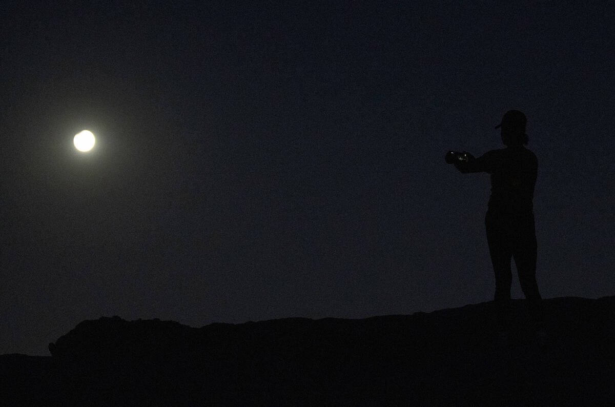 A woman takes a photograph during the Harvest Moon Supermoon partial lunar eclipse at Lone Moun ...