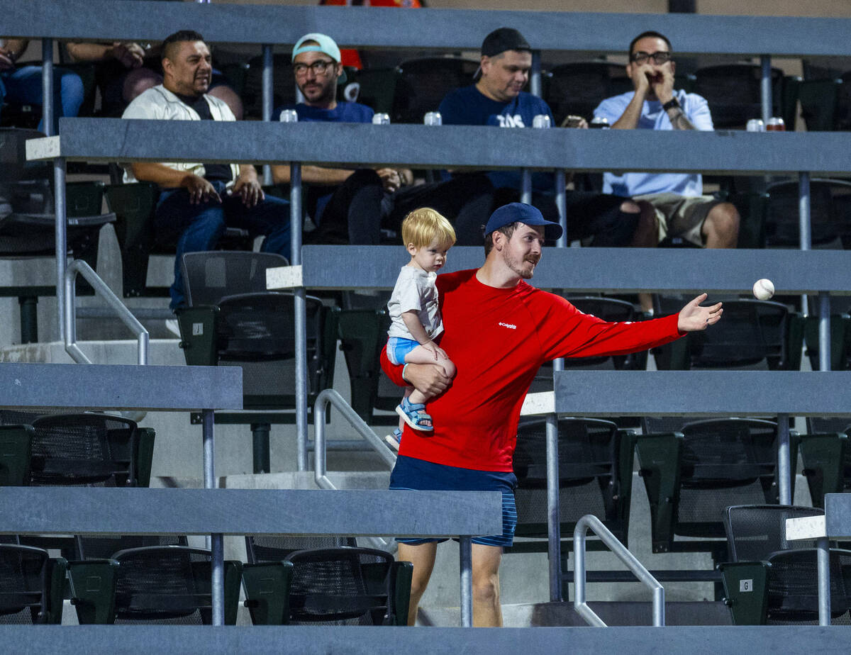 A fan catches a baseball while holding his son as the Aviators battle the El Paso Chihuahuas du ...