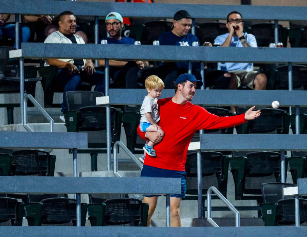 A fan catches a baseball while holding his son as the Aviators battle the El Paso Chihuahuas du ...