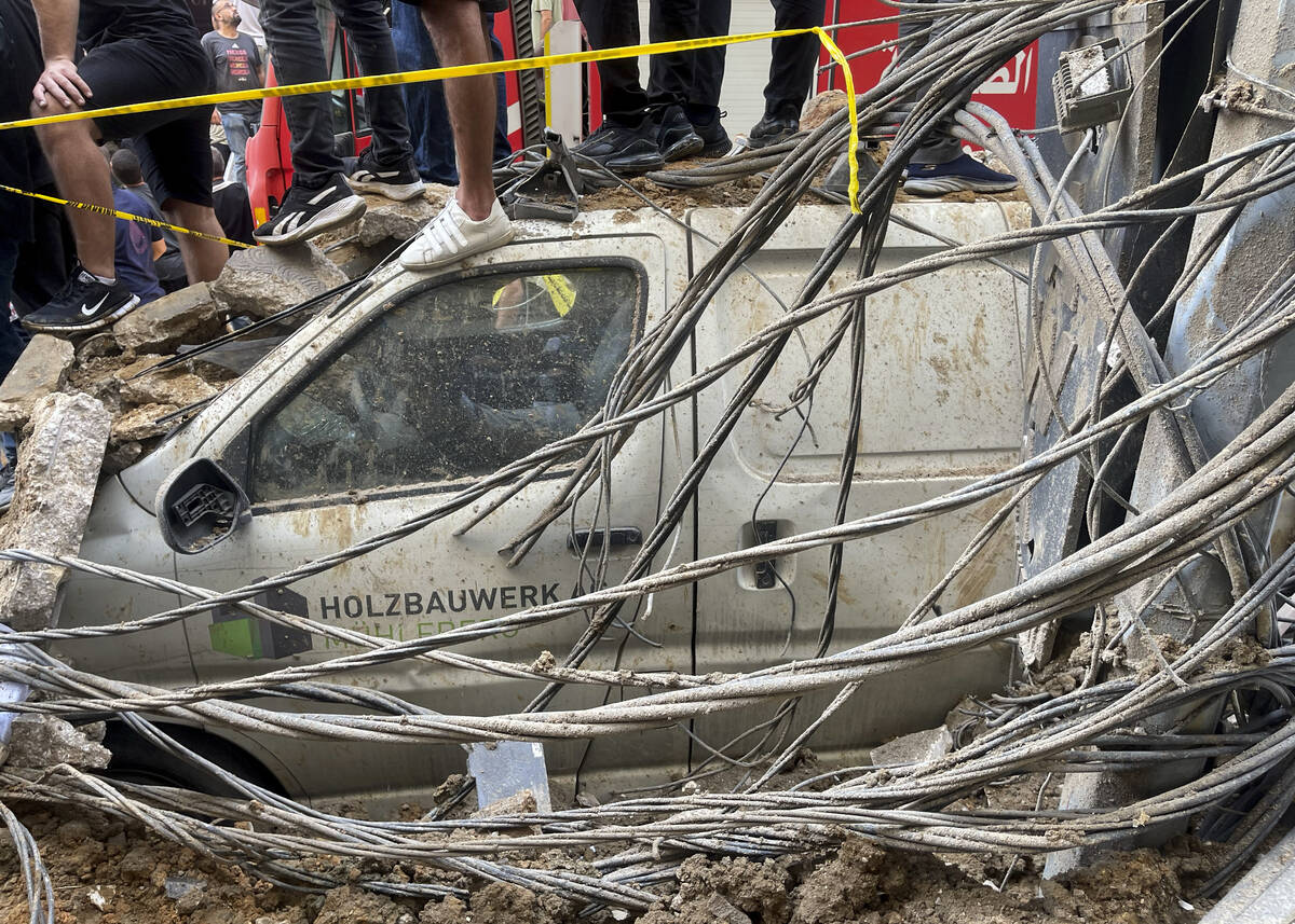 People stand on top of a damaged car at the scene of a missile strike in the southern suburbs o ...