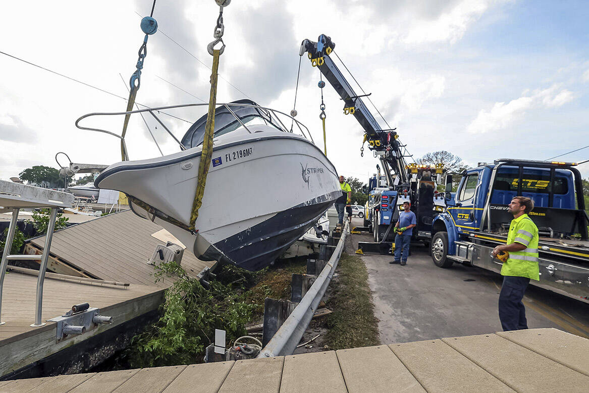 Crews raise a boat from the side of the road after it was pushed by floodwaters from Hurricane ...