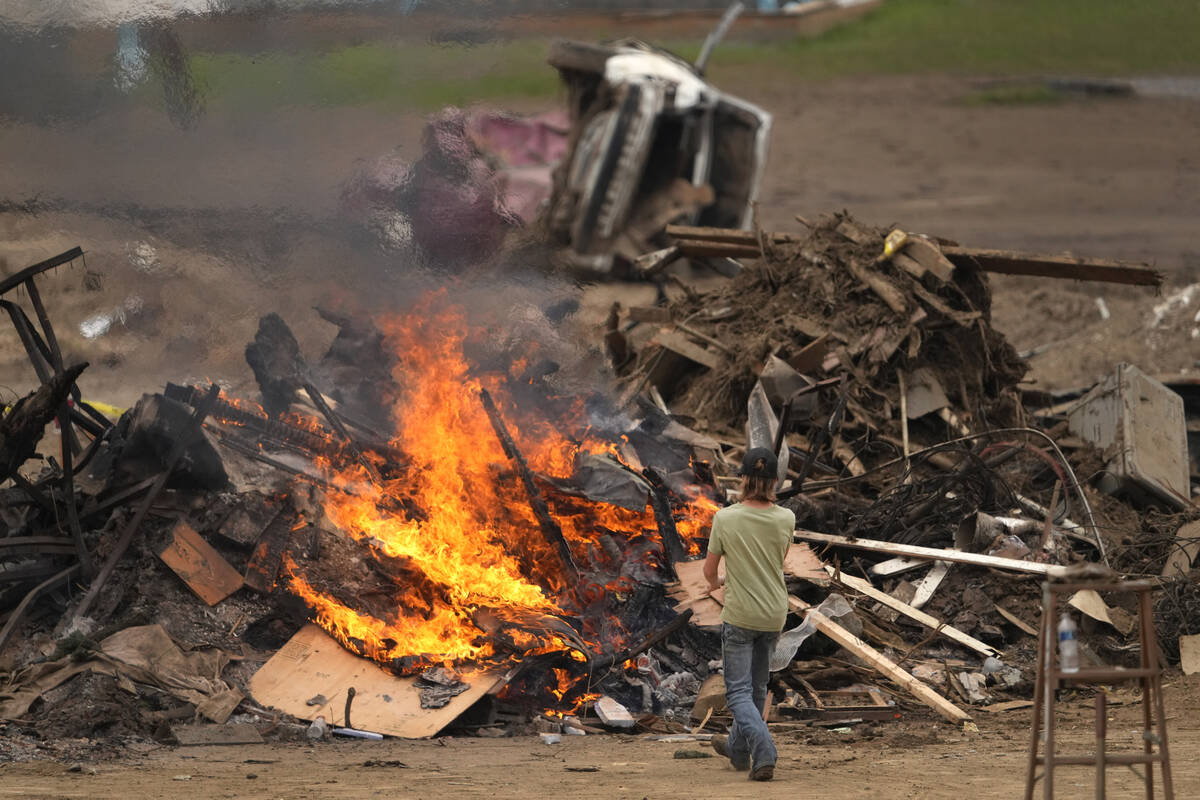 A person throws objects on a burning debris pile in the aftermath of Hurricane Helene, Friday, ...