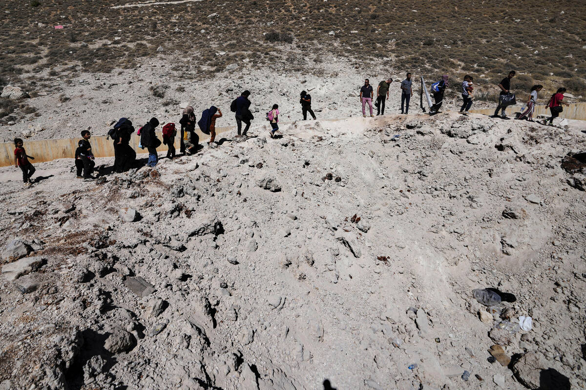 People carry their luggage as they cross into Syria on foot, through a crater caused by Israeli ...