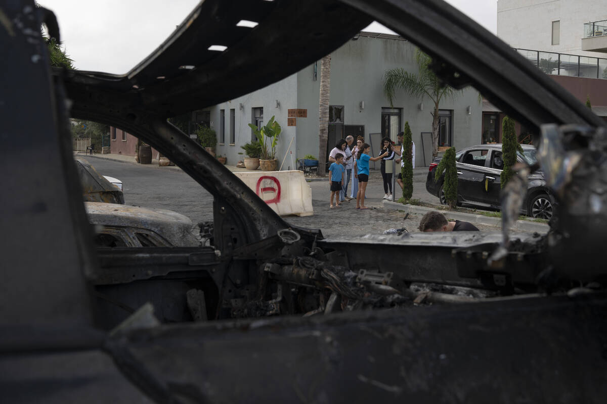 People stand next to burnt and damaged cars after a rocket, launched from Lebanon, hit an area ...