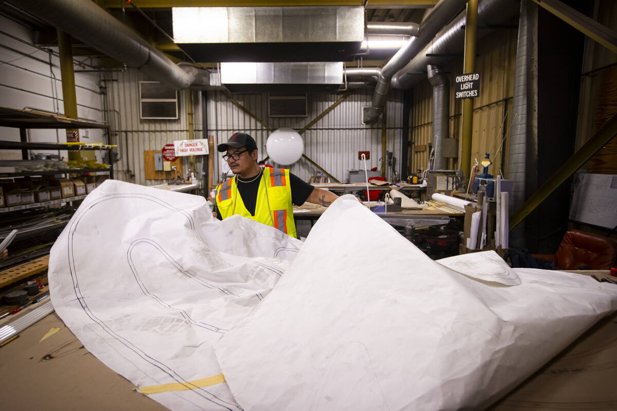 YESCO neon bender Oscar Gonzalez opens a massive sheet of paper with a diagram to work on the r ...