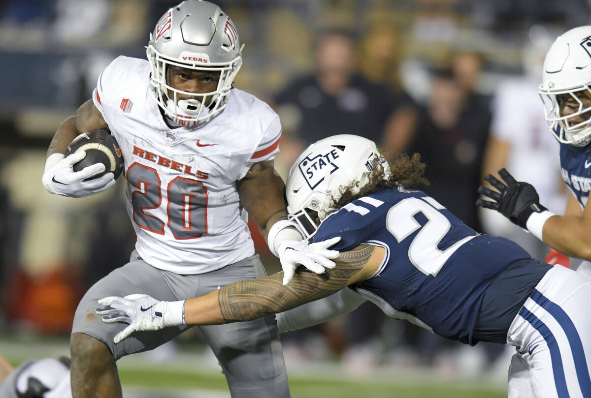 UNLV running back Kylin James (20) carries the ball as Utah State linebacker Logan Pili (27) de ...