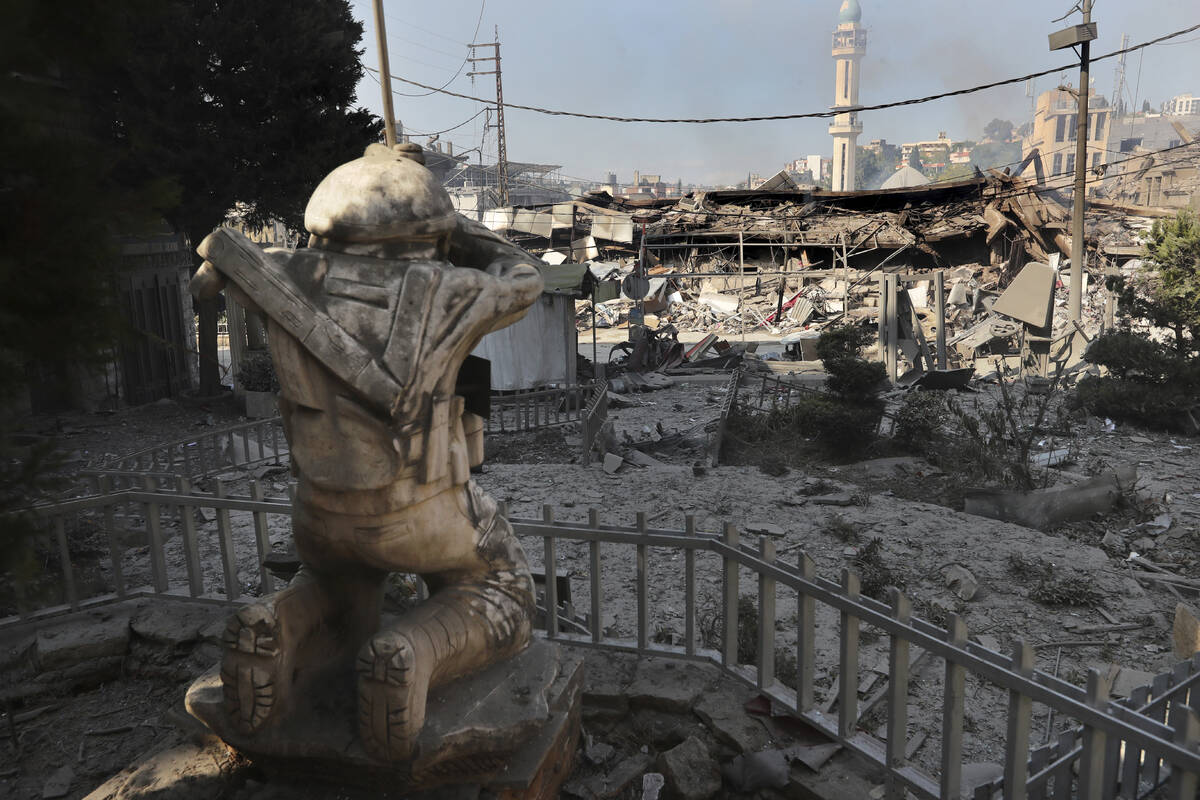 Destroyed shops are seen in front of a Hezbollah fighter statue on a commercial street that was ...