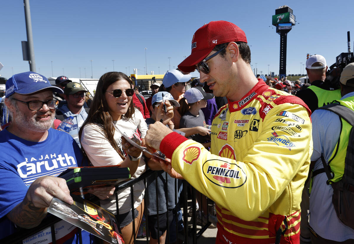 Joey Logano, right, gives autographs before a NASCAR Cup Series auto race at Kansas Speedway in ...