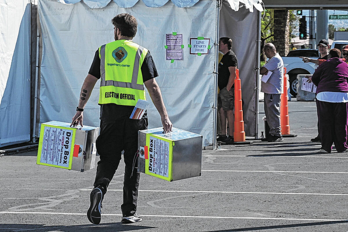 An election official carries empty ballot drop boxes to a polling place on Blue Diamond Road on ...