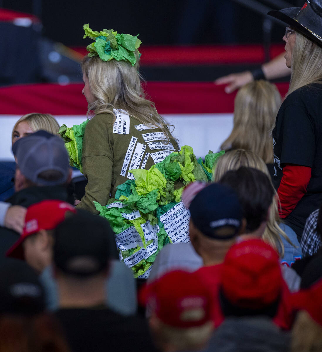 A supporter with a word salad costume takes her seat before former President Donald Trump arriv ...