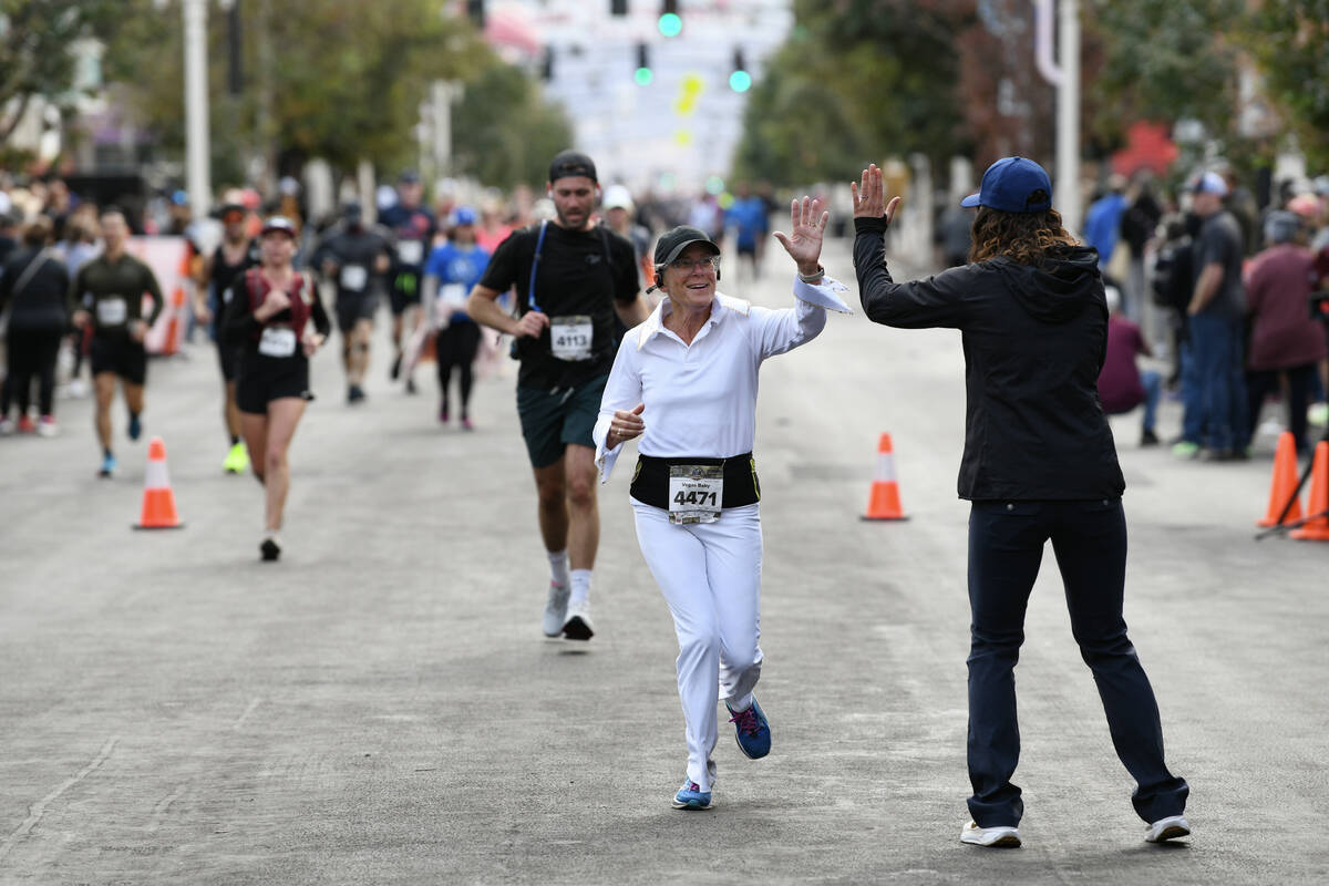 A participant dressed as Elvis gets a high five from the race announcer as she approaches the f ...