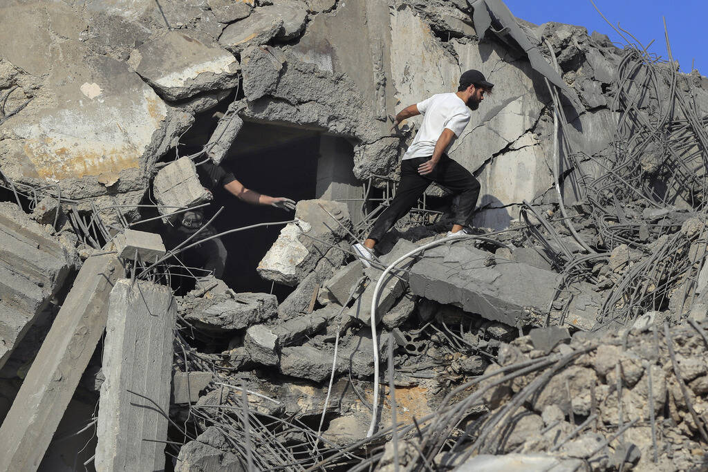 People search for victims at a destroyed building hit in an Israeli airstrike, in Ghaziyeh town ...