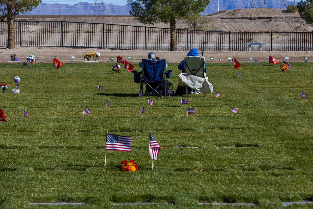 Visitors sit amongst a few of the 14,000 small American flags at veterans grave markers placed ...