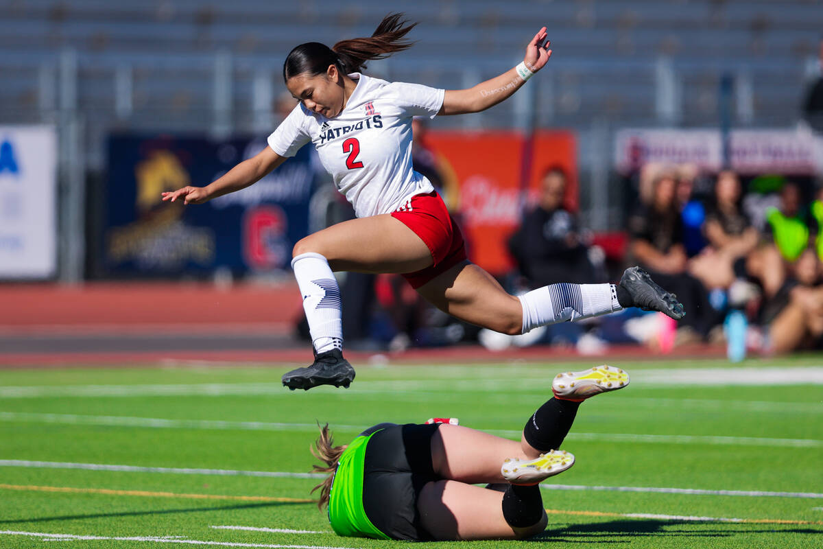 Liberty midfielder Natalie Collins (2) jumps over Faith Lutheran goalkeeper Olivia Petty (99) a ...