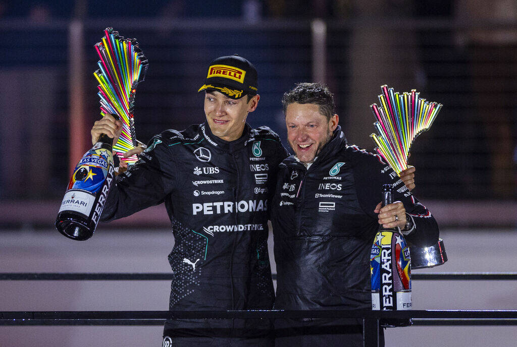 Mercedes driver George Russell and a team member collect the winner's and team trophies atop th ...