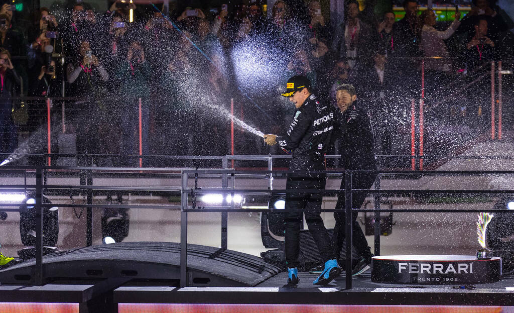 Mercedes driver George Russell and a team member spray champagne at each other atop the podium ...