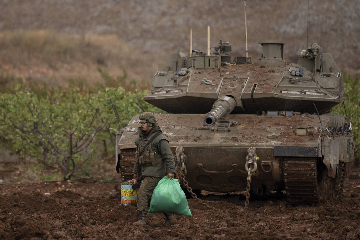 An Israeli soldier walks past a tank in an area near the Israeli-Lebanese border, as seen from ...