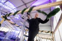 Elizabeth Thrailkill wraps garland around a vendor booth during setup of Christmas on the Strip ...