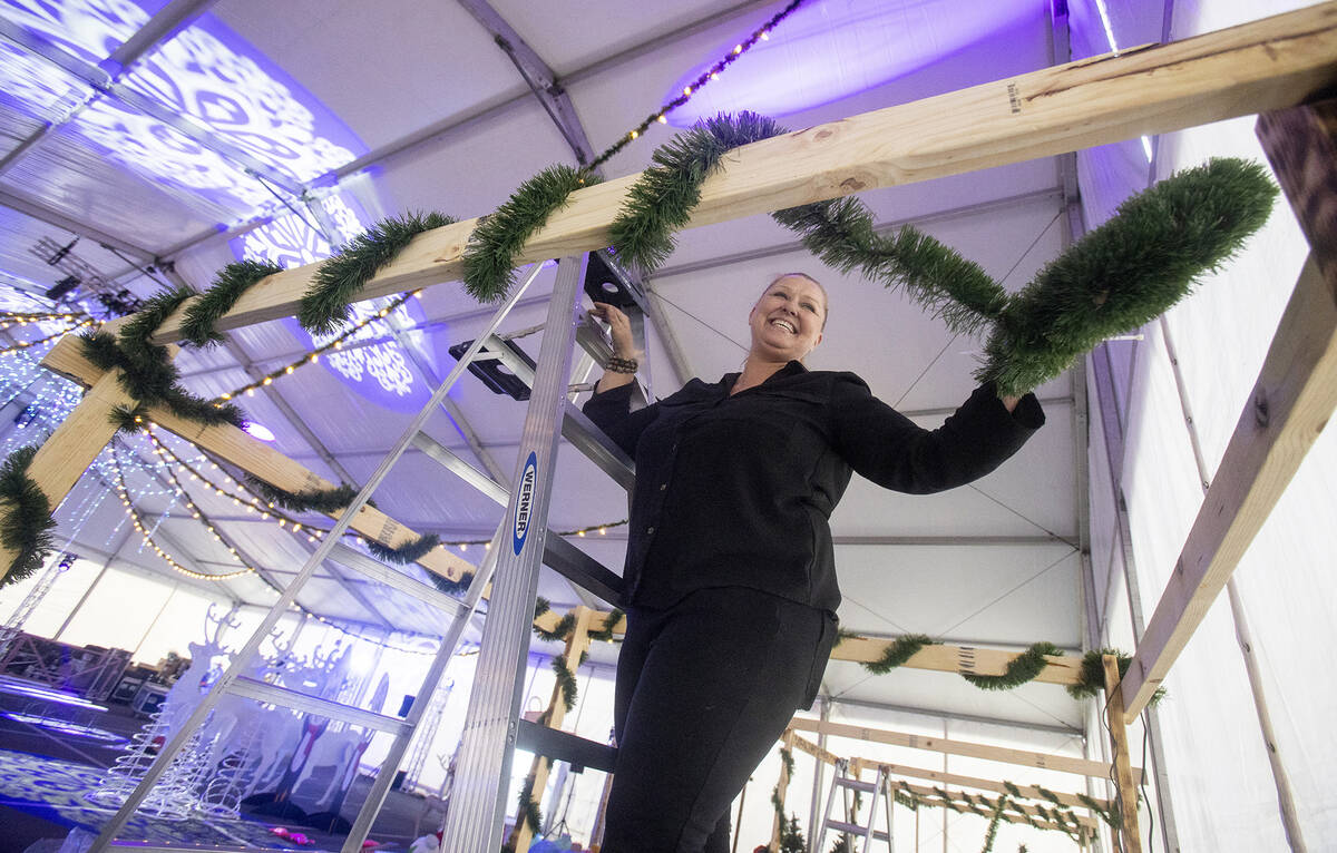 Elizabeth Thrailkill wraps garland around a vendor booth during setup of Christmas on the Strip ...