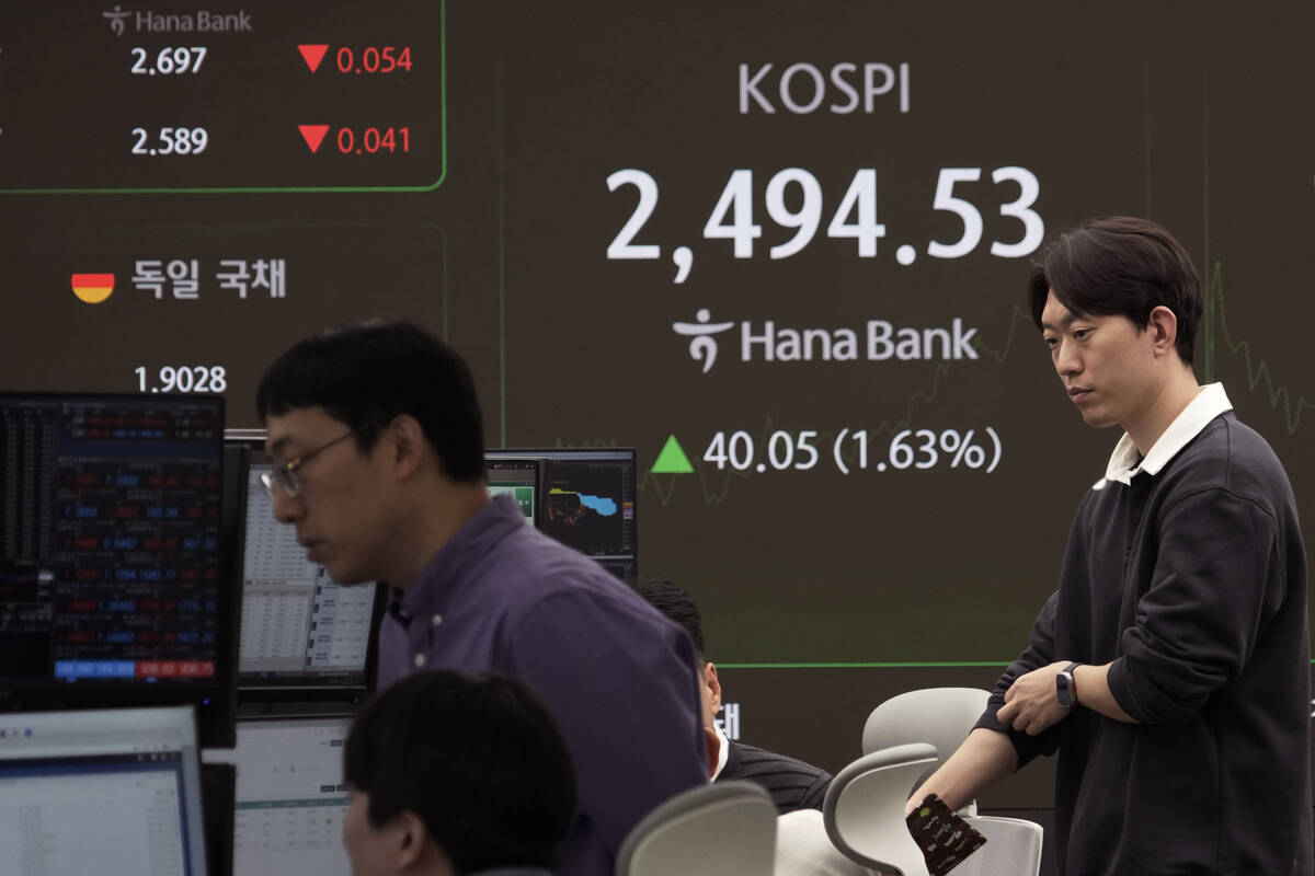 Currency traders work near a screen showing the Korea Composite Stock Price Index (KOSPI) at th ...