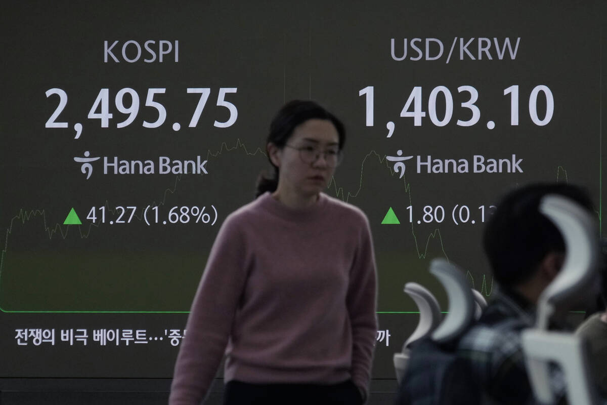 A currency trader passes by a screen showing the Korea Composite Stock Price Index (KOSPI), lef ...