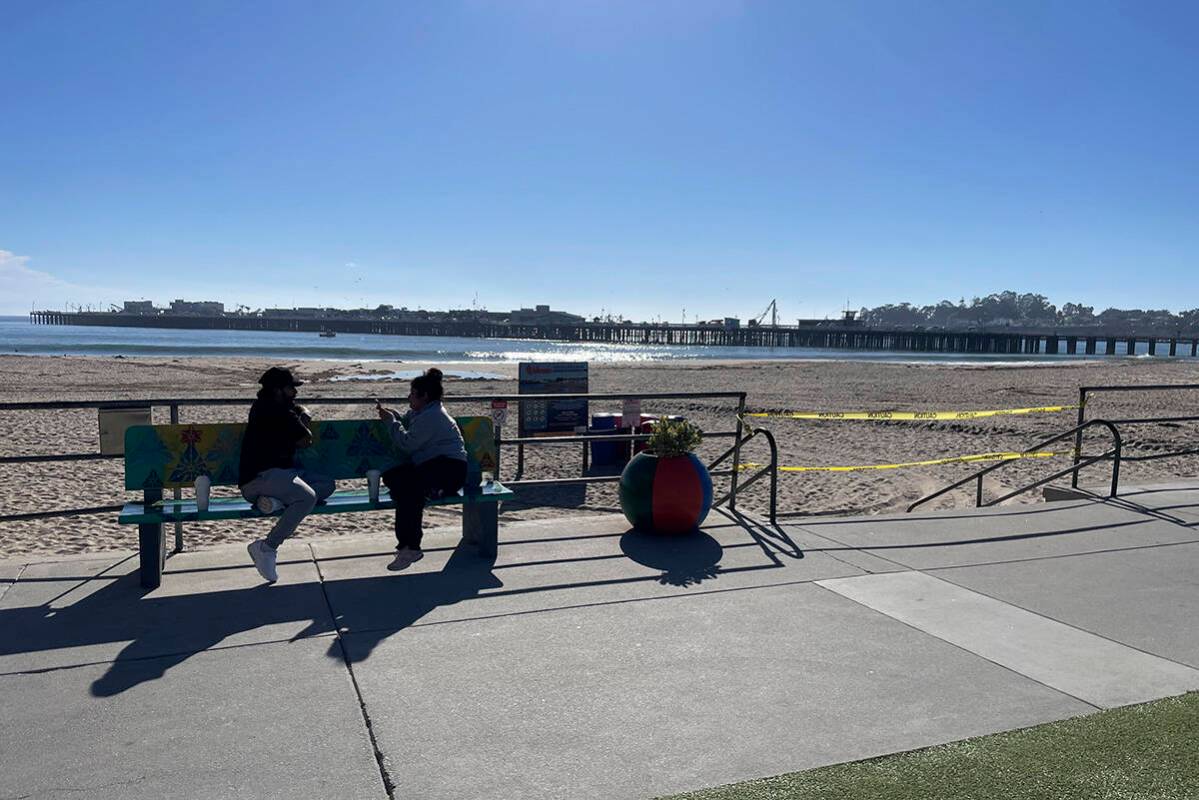 People sit on a bench along the beach in Santa Cruz, Calif. after authorities cleared the main ...