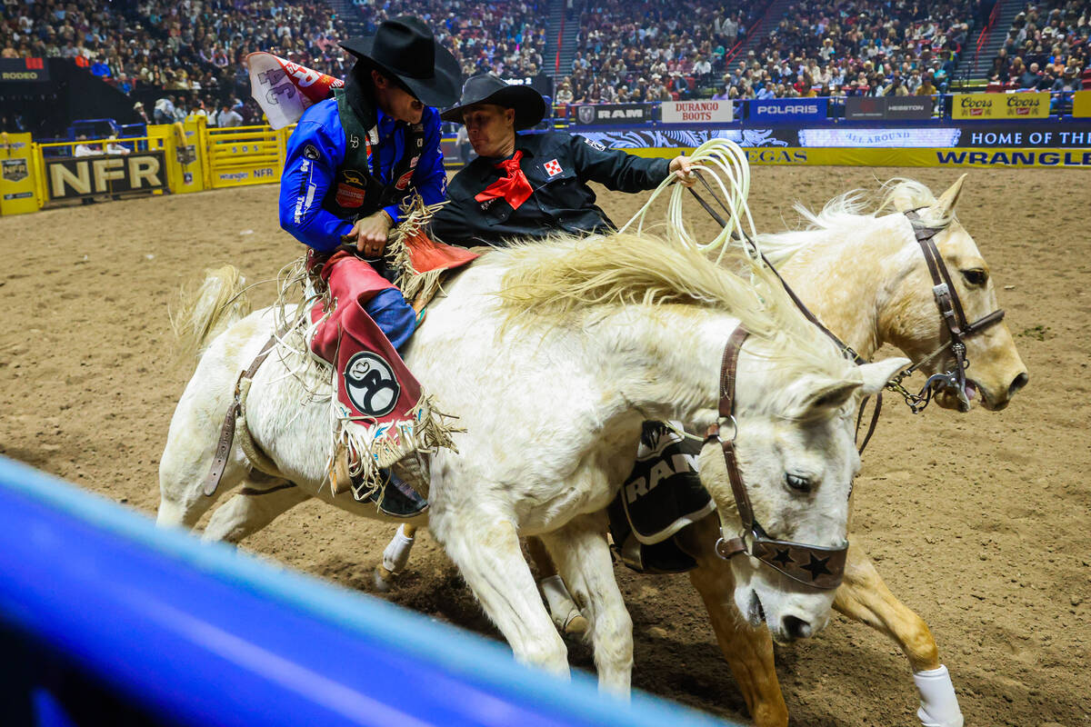 Bareback rider Leighton Berry gets help from a pickup man after his ride during round three of ...