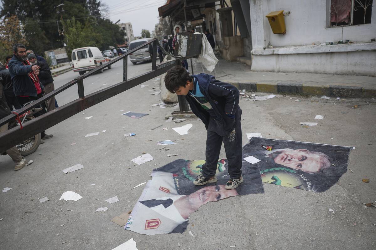 A boy steps over pictures of Syrian President Bashar Assad and his late father, Hafez Assad, ri ...