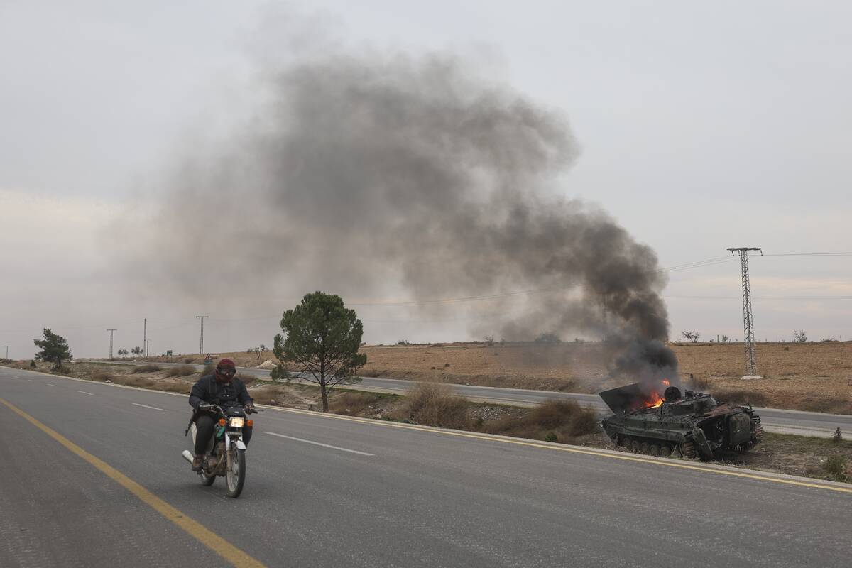 A man rides his motorcycle past a burning government armoured vehicle south of Hama, Syria, Sat ...