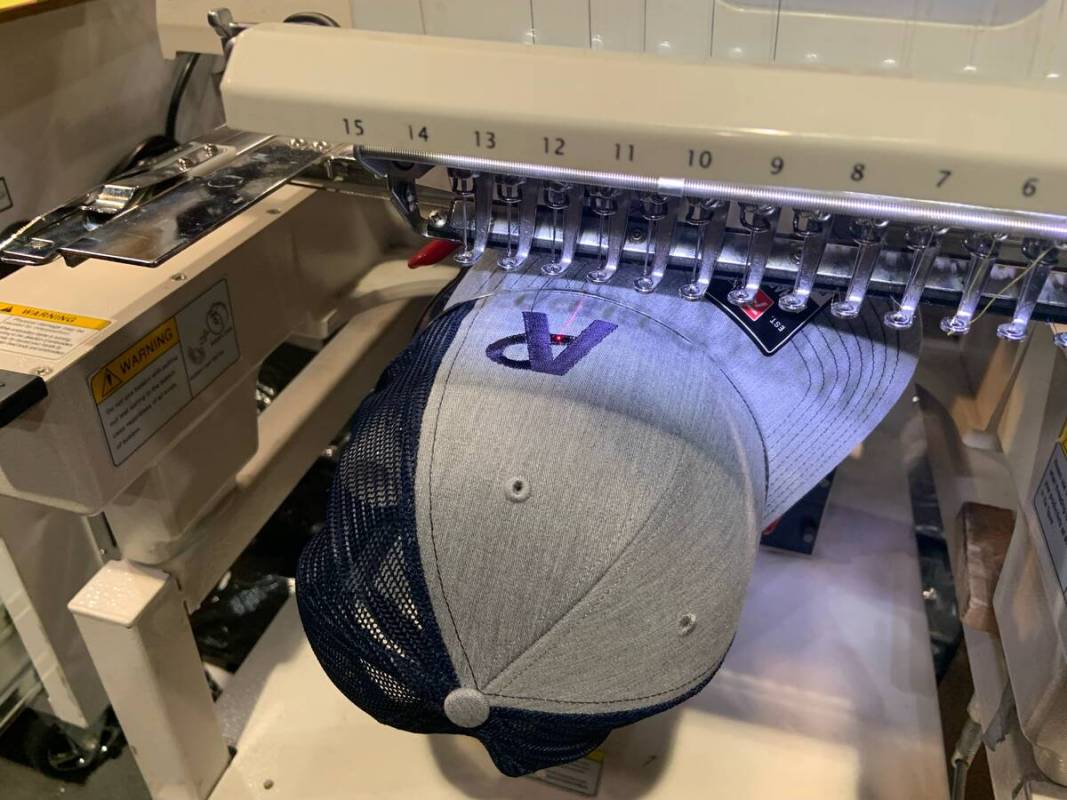 A baseball cap runs its way through one of Cattilac Style's embroidery machines, placing a pers ...