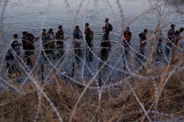 FILE - Migrants wait to climb over concertina wire after they crossed the Rio Grande and entere ...