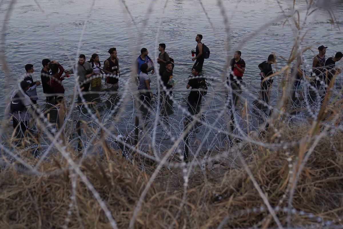 FILE - Migrants wait to climb over concertina wire after they crossed the Rio Grande and entere ...