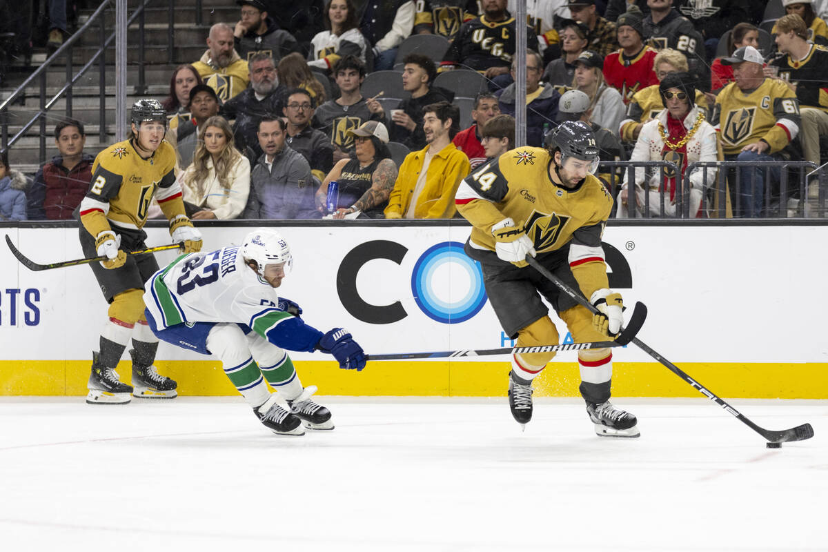 Golden Knights defenseman Nicolas Hague (14) keeps the puck from Vancouver Canucks center Teddy ...