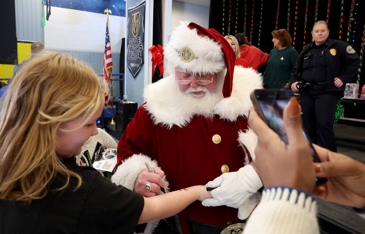 Ariel Burge gets an autograph from Santa during a holiday party at Sewell Elementary School in ...