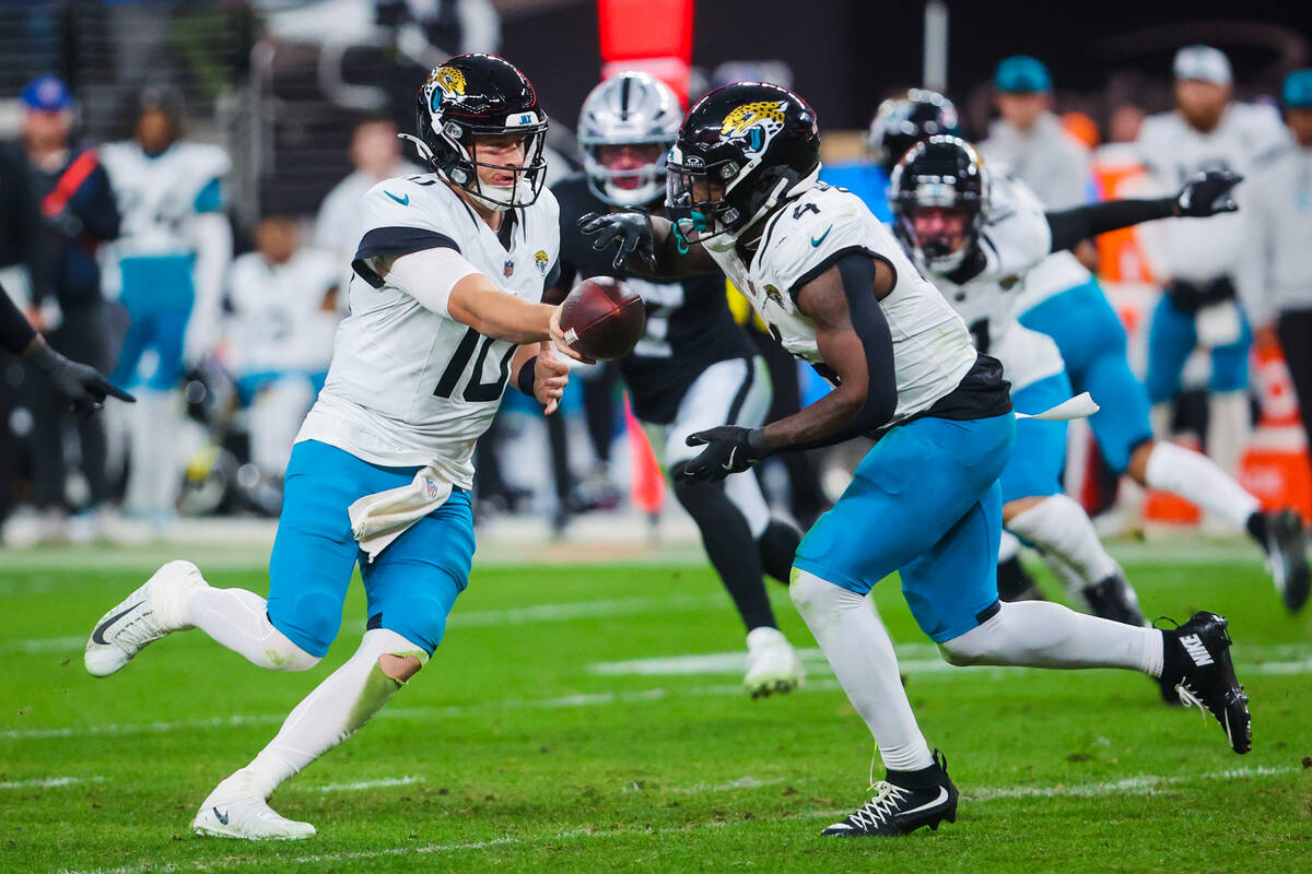 Jacksonville Jaguars quarterback Mac Jones (10) passes the ball off to Jacksonville Jaguars run ...