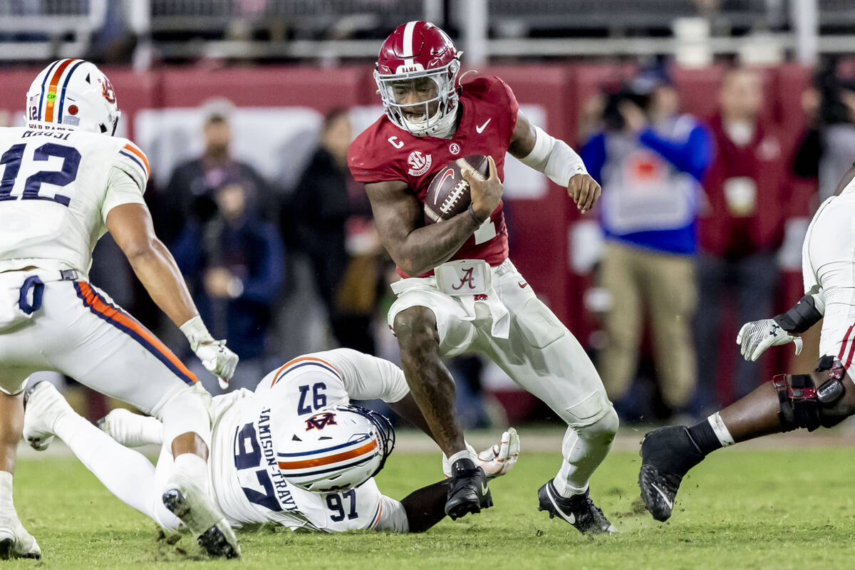 Alabama quarterback Jalen Milroe (4) eludes Auburn defensive lineman Quientrail Jamison-Travis ...