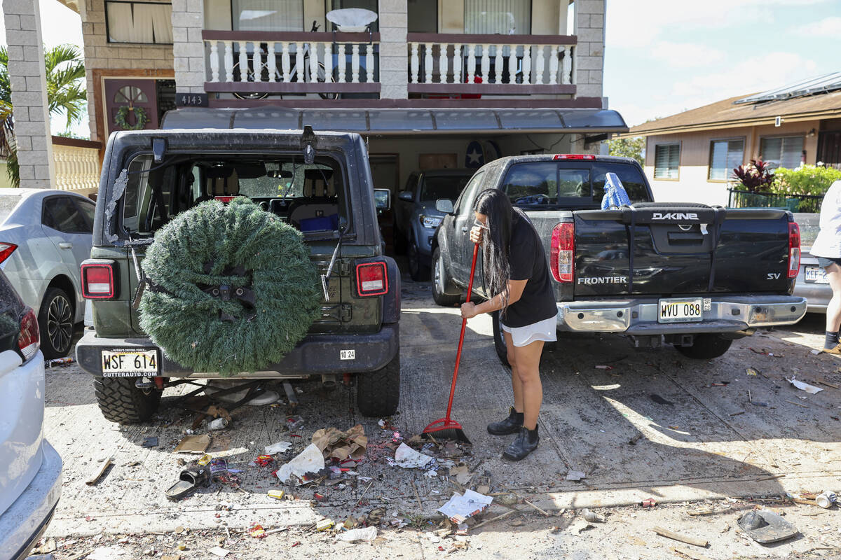 A woman sweeps debris from a driveway across the street from the home where a New Year's Eve fi ...