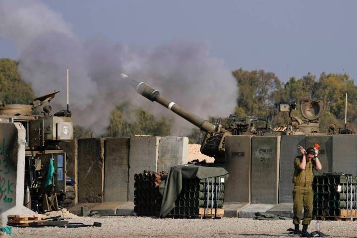 An Israeli soldier covers his ears as an artillery gunner fires into the Gaza Strip from a posi ...