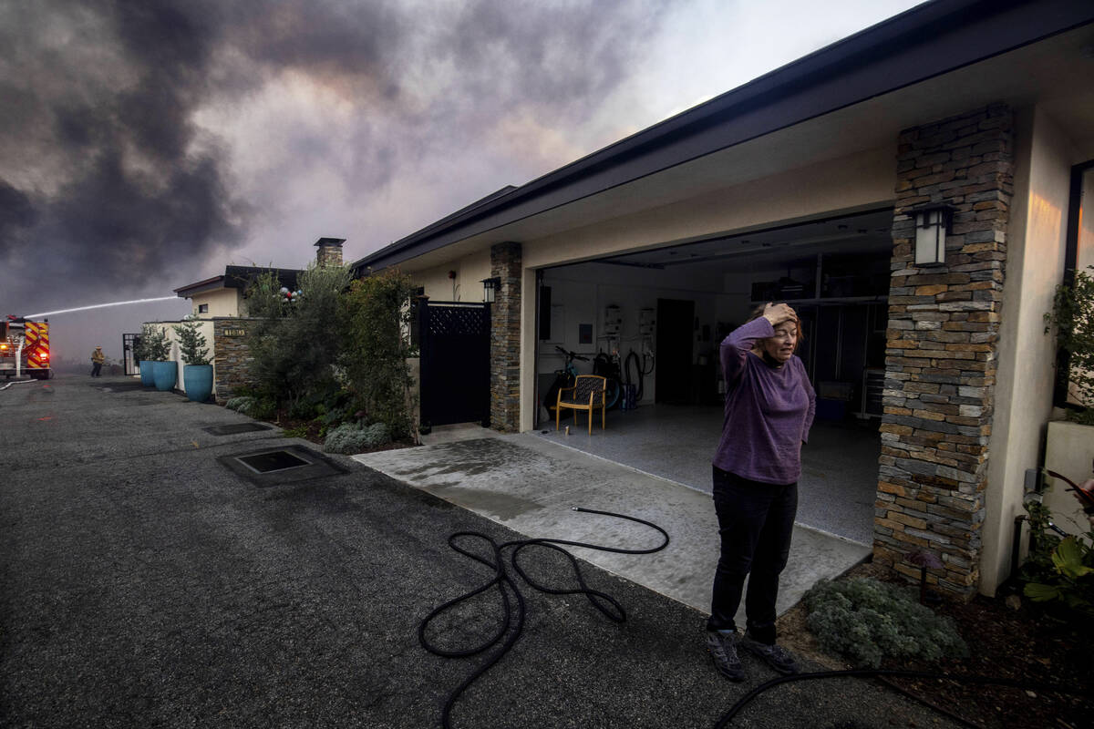 A resident stands in front of a garage as fire crews fight the Palisades Fire nearby in the Pac ...