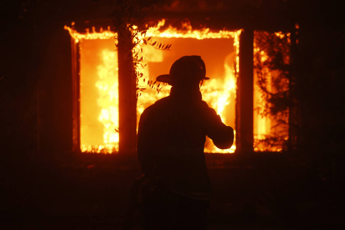 A firefighter is silhouetted in front of a burning structure as the Palisades Fire sweeps throu ...