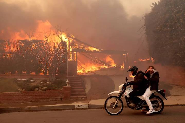 Two people ride past a burning house off Enchanted Way in the Marquez Knolls neighborhood of Pa ...